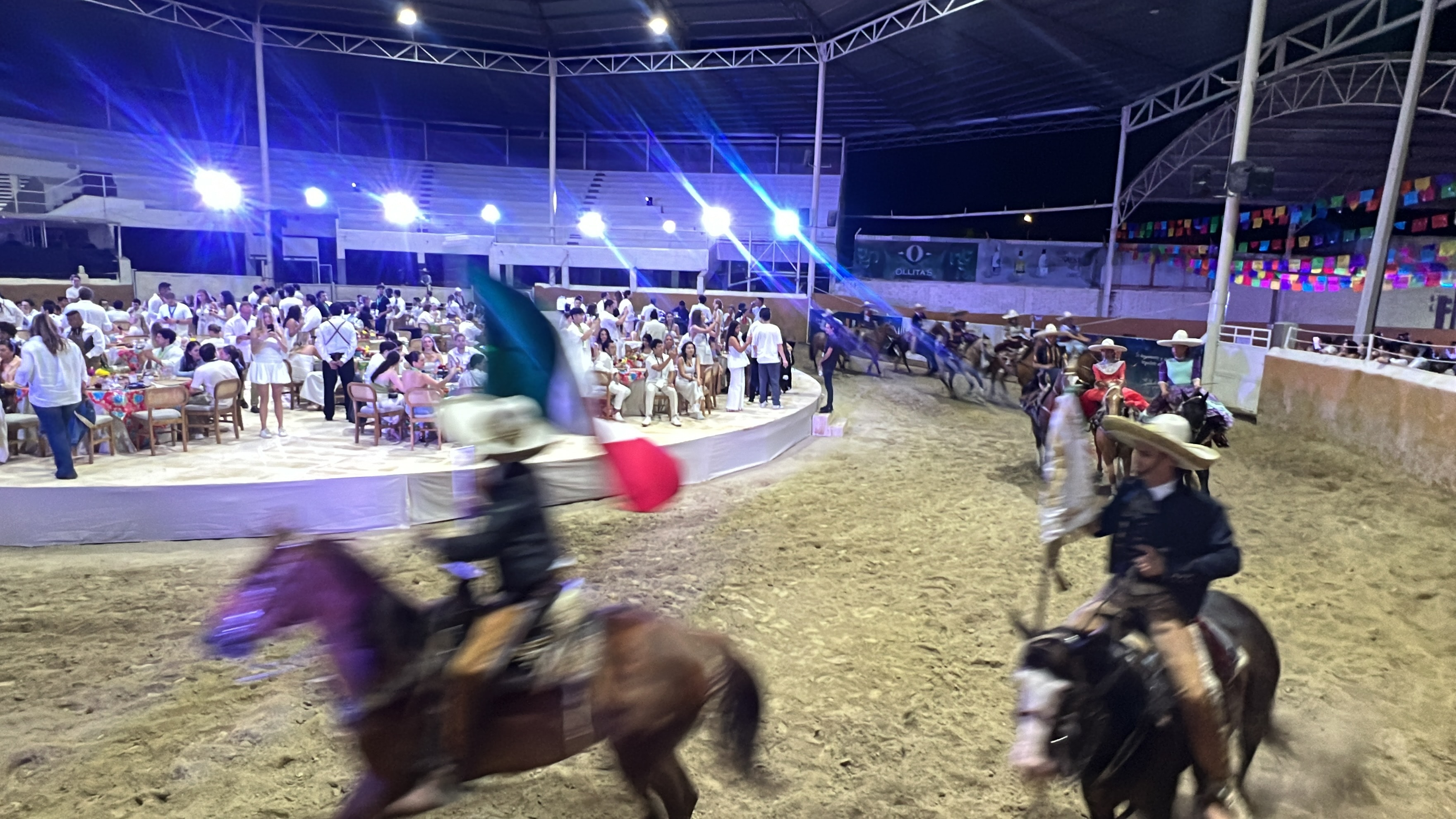 Charros a caballo con bandera mexicana durante cena de gala nocturna