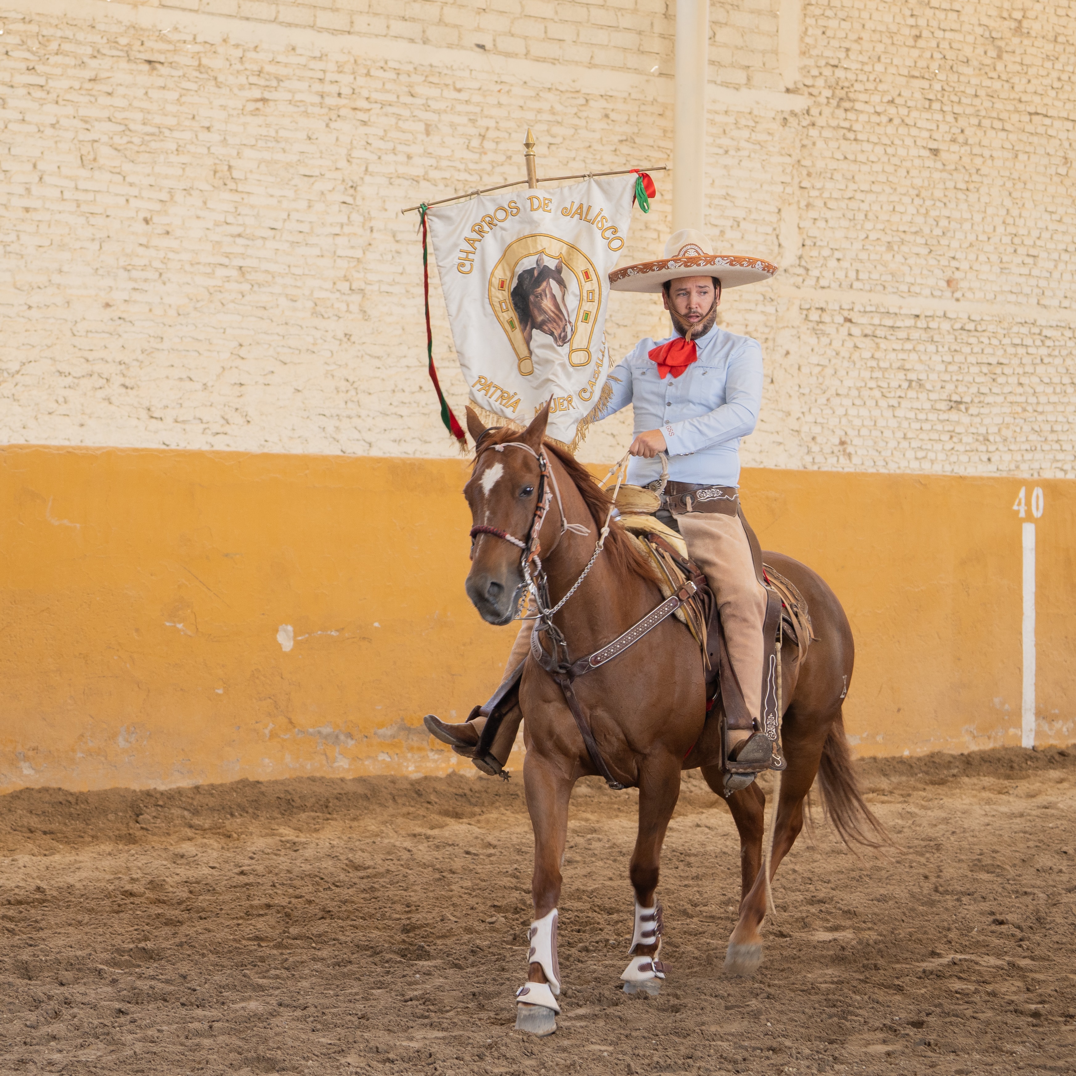 Charro a caballo portando la bandera de Charros de Jalisco en el Lienzo Charro