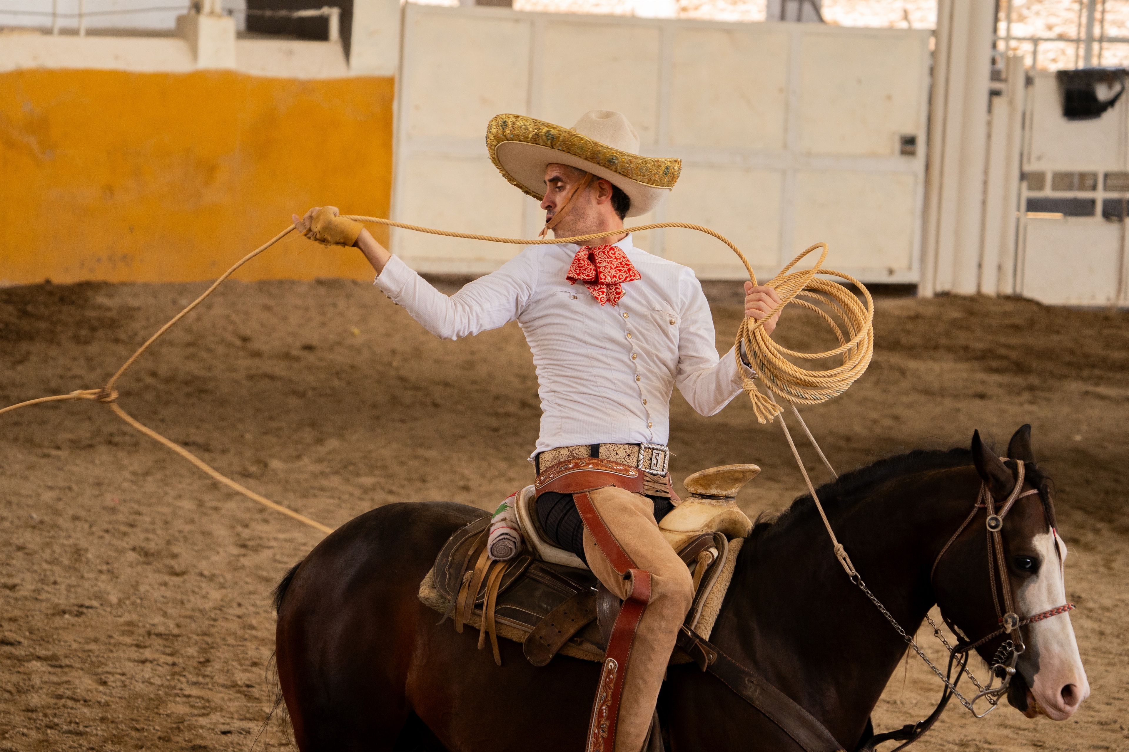 Charro ejecutando mangana con reata doble montado en caballo negro en el Lienzo Charro