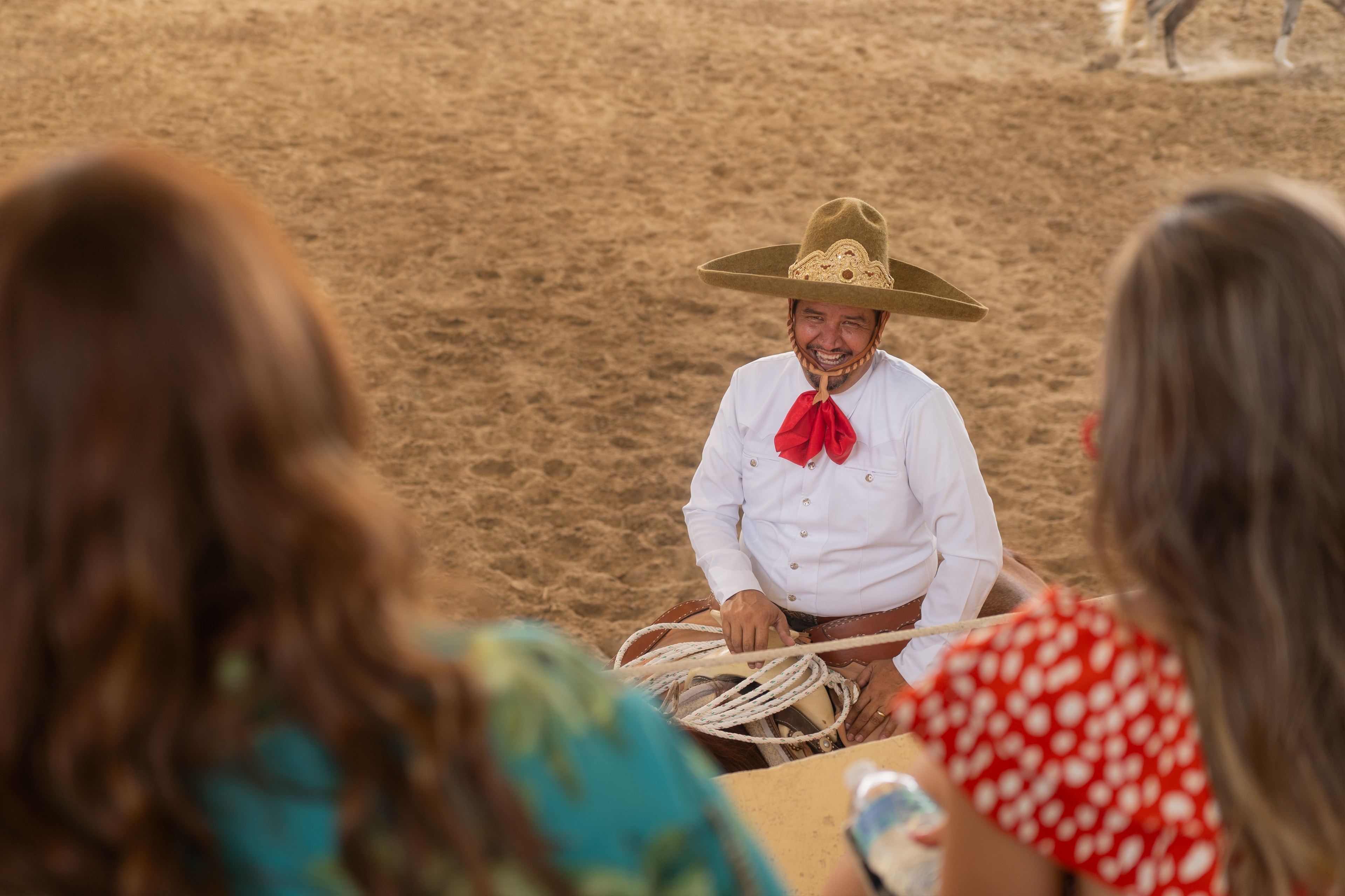 Charro sonriente con reata interactuando con turistas en el Lienzo Charro