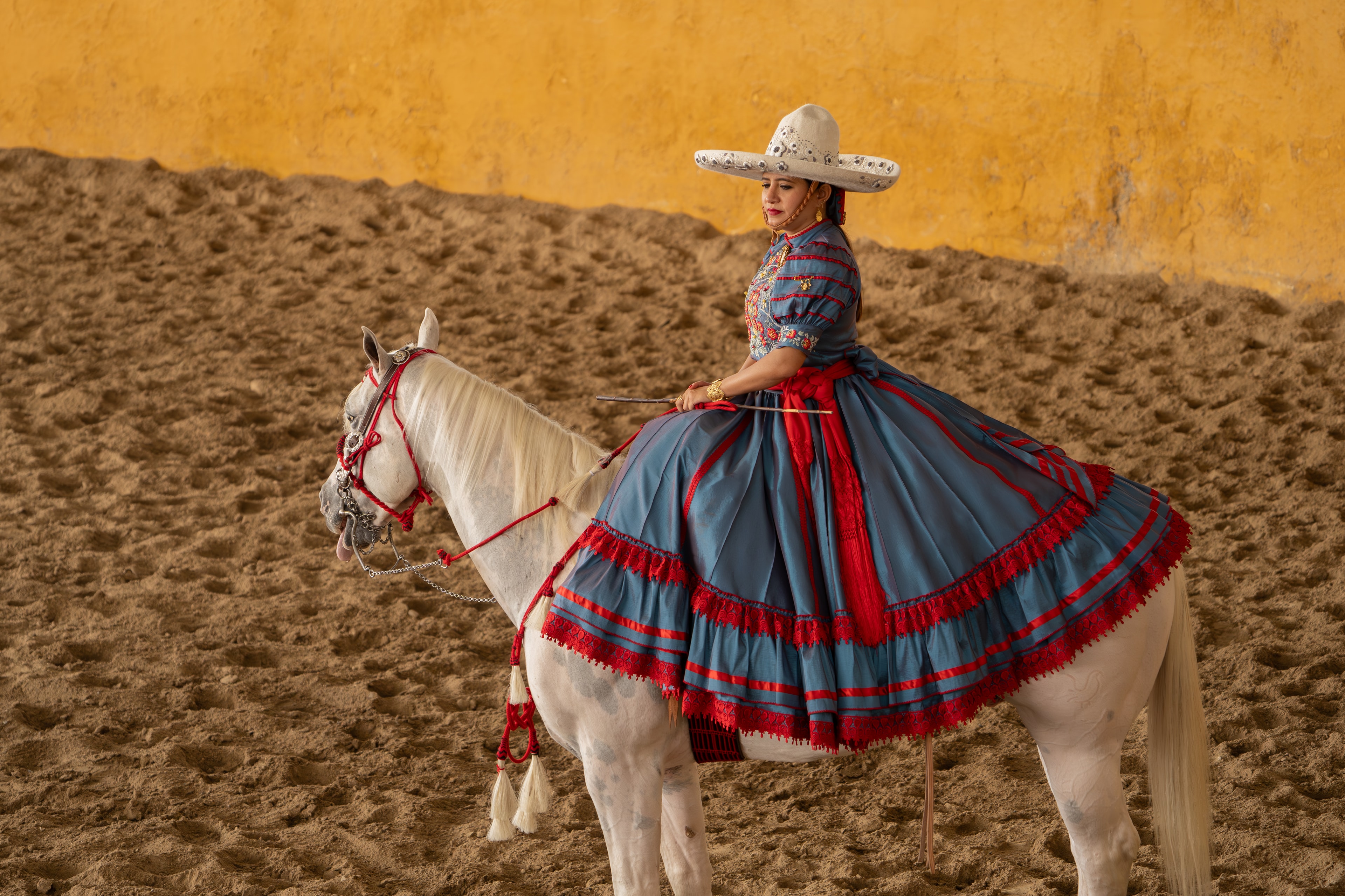Escaramuza con traje azul y rojo posando sobre caballo blanco en el Lienzo Charro
