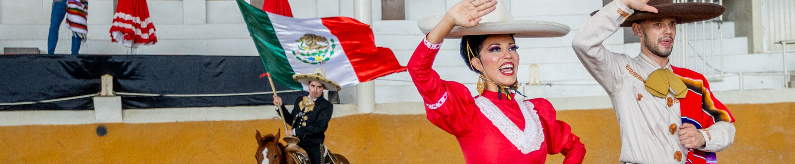 Pareja de charros a caballo con bandera mexicana en el Lienzo Charro
