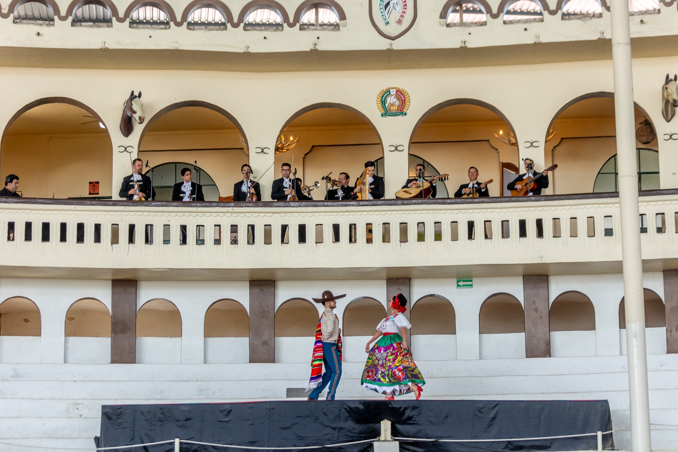 Grupo de invitados aplaudiendo baile folklórico con mariachi en balcón del Lienzo Charro